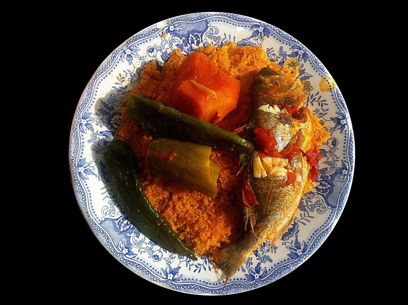 Un piatto di cuscus di pesce con verdure e pesce intero cotto nel sugo