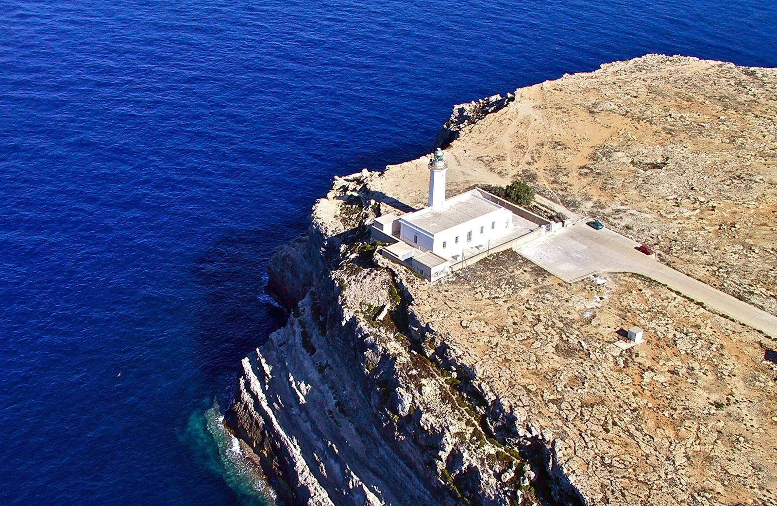 Un faro bianco su una scogliera a picco sul mare blu di Lampedusa